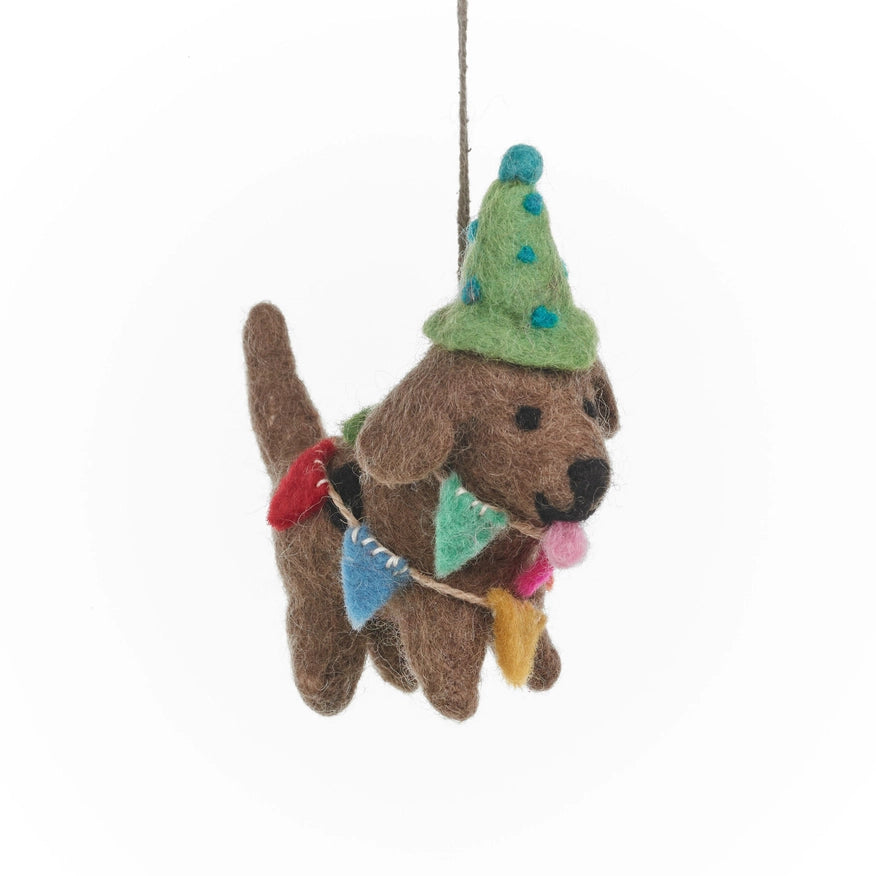 A handmade felt brown dog is shown dressed for a party. It is wearing a green party hat with blue polka dots and a multicolored party bunting around its neck.