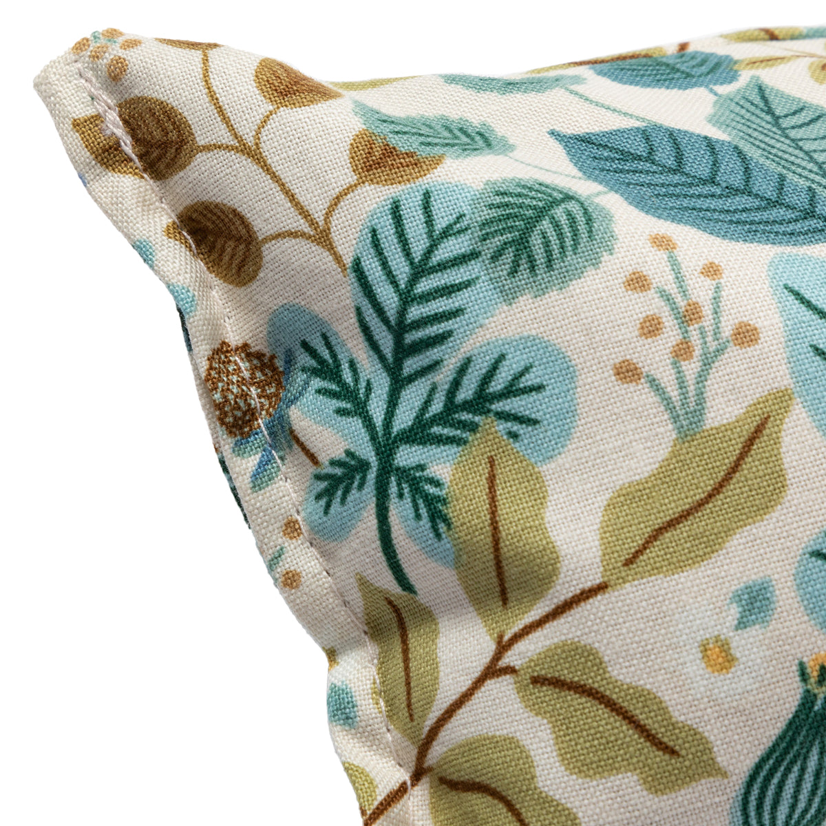 A close-up of a botanical-patterned eye pillow. Visible details include stitching along the seam and a pattern of teal leaves and brown berries.