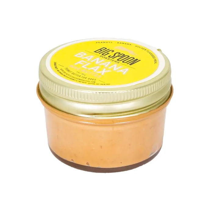 A glass jar of Big Spoon Roasters Wag Butter Banana Flax. It has a gold lid and a yellow label on a white background.