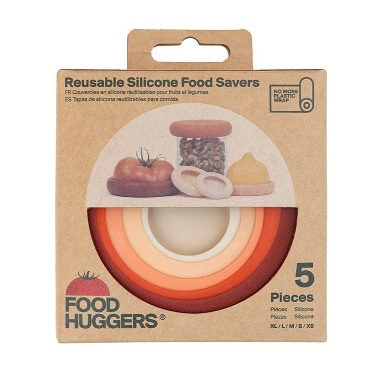 A cute box of "Food Huggers" reusable silicone food savers is shown with a window revealing a set of five in a gradient of earthy tones. The box says "No More Plastic Wrap" on the side, highlighting the product's sustainable mission.
