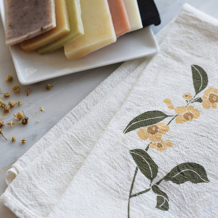 A lovely white cotton napkin is decorated with a playful pattern of monarch butterflies and delicate orange and pink flowers with soft green leaves.