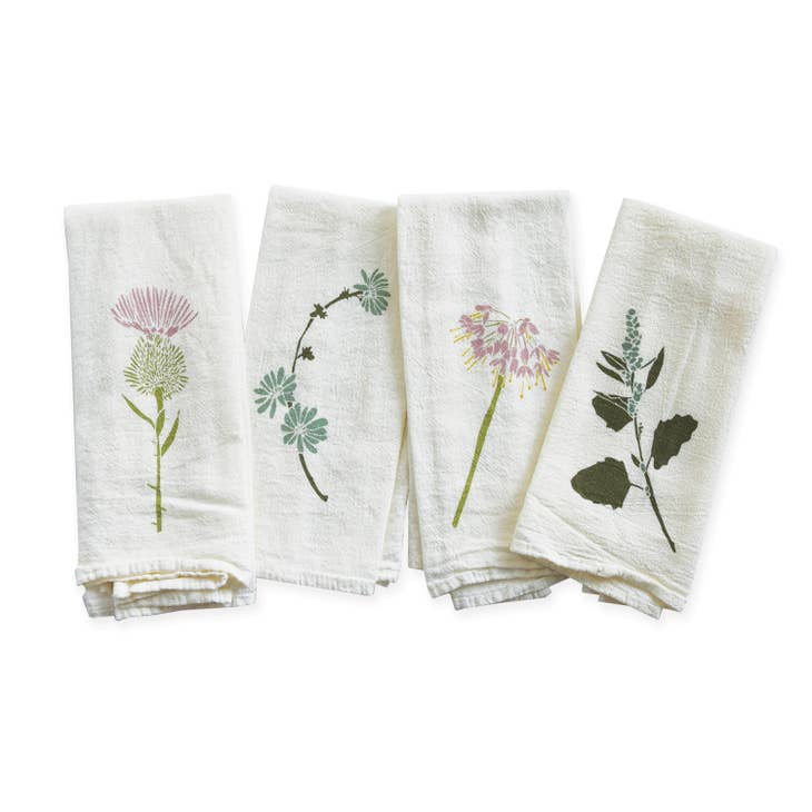 A sweet set of four white cotton napkins is shown folded, each featuring a different whimsical botanical print of flowers and leaves in shades of pink, green and blue.