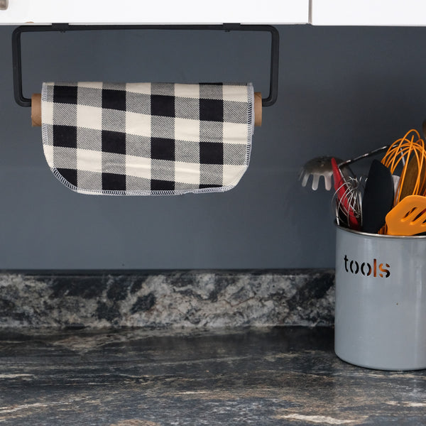 A single black and white buffalo check Cheeks Ahoy unpaper towel is shown on a paper towel holder under a kitchen cabinet.