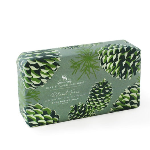 A rectangular 'Soap & Paper Factory' shea butter soap bar wrapped in sage-green paper with a pattern of pine cones. The label reads "Roland Pine, siberian fir, pine & cilantro."