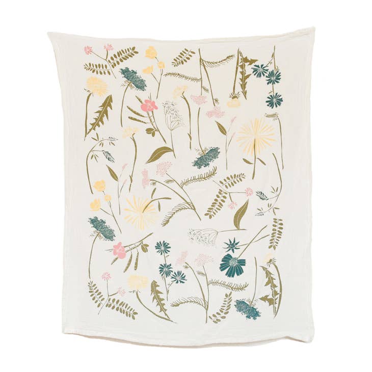 A white kitchen towel features a whimsical pattern of different wildflowers, with blossoms in soft pink, yellow, teal and delicate green stems.