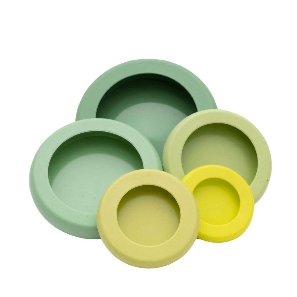 A set of 5 reusable silicone food savers are stacked in a pyramid shape. The savers come in a gradient of colors from dark green to yellow, with each one slightly different in size.