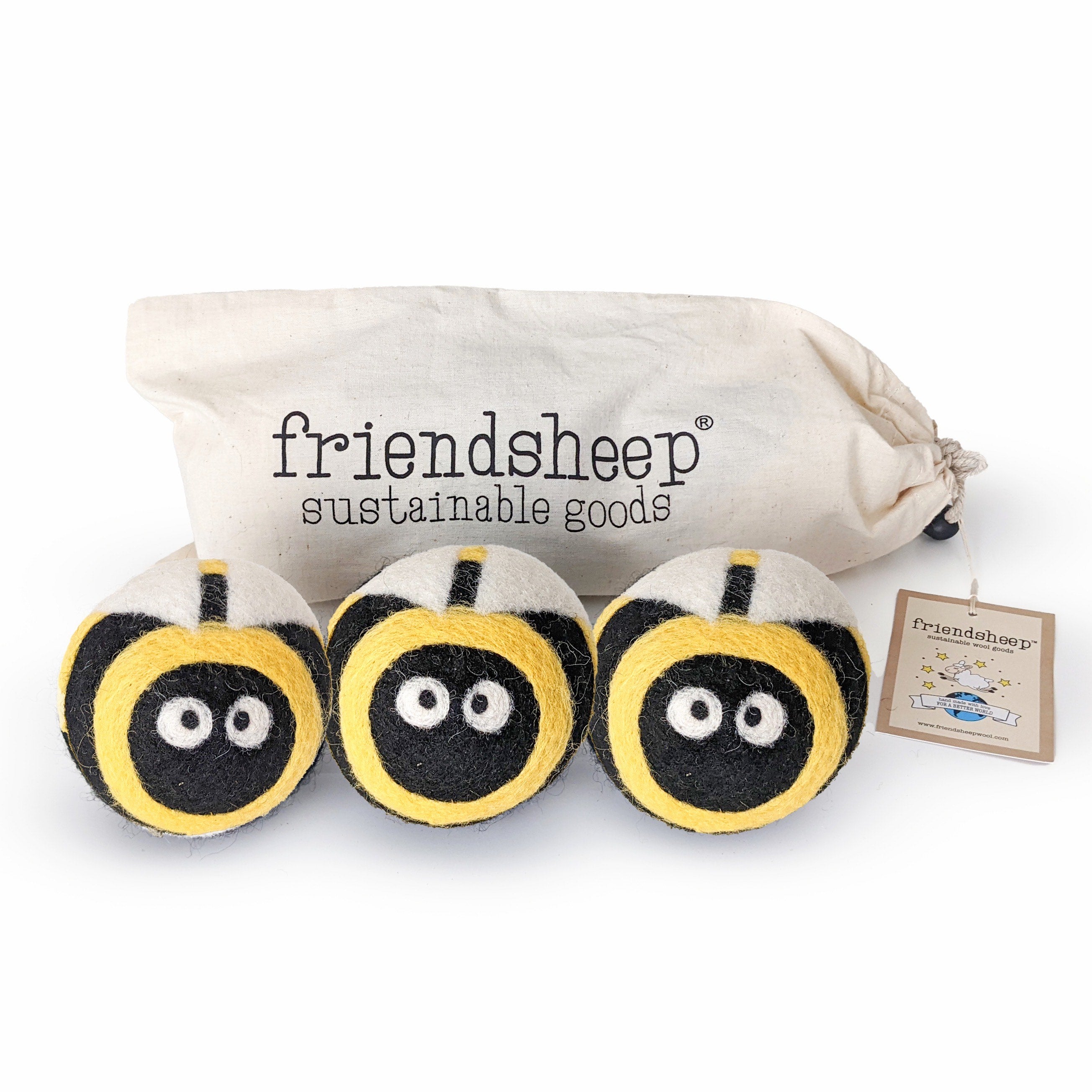 A set of three Friendsheep sustainable goods wool dryer balls are shown, each decorated with a cute bee face. They are sitting in front of their white canvas drawstring bag.