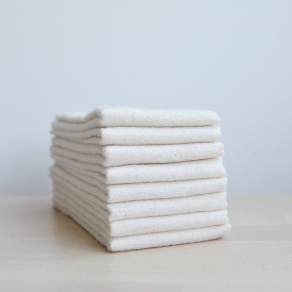 A stack of multiple folded off-white towels is shown on a light-colored surface. The towels are stacked neatly and have no visible branding.