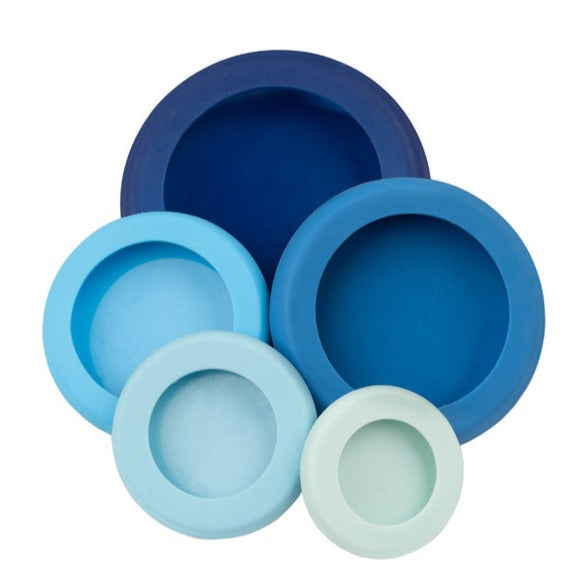 A set of 5 reusable silicone food savers are stacked in a pyramid shape. The savers come in a gradient of colors from light green to dark blue, with each one slightly different in size.