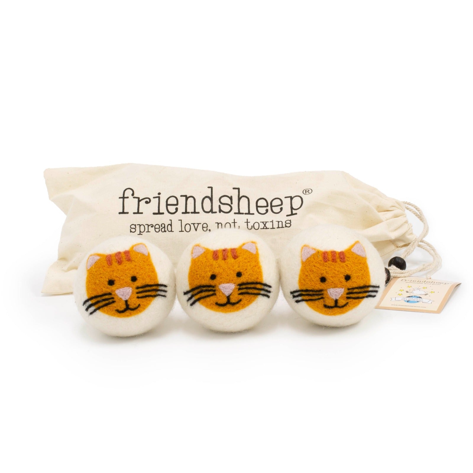 A set of three Friendsheep sustainable goods wool dryer balls are shown, each decorated with an orange cat face. The dryer balls are sitting in front of their white canvas drawstring bag.