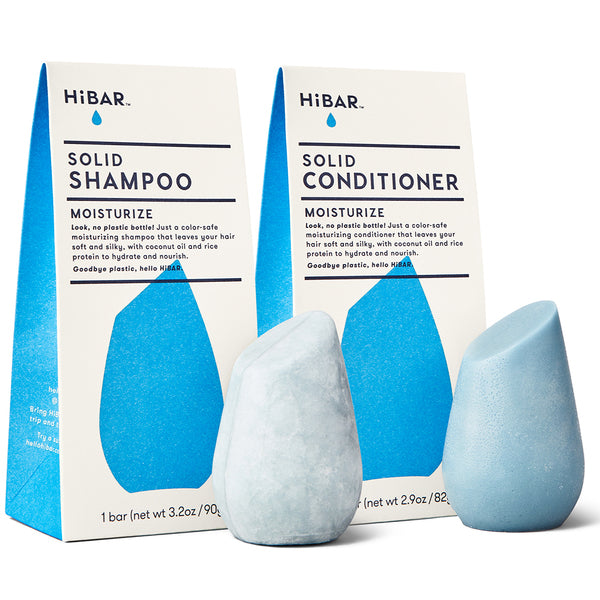 Two HiBar MOISTURIZE solid hair care products: a light blue shampoo bar next to a light blue conditioner bar and its matching boxes, emphasizing no plastic, coconut oil, and rice protein for hydration.