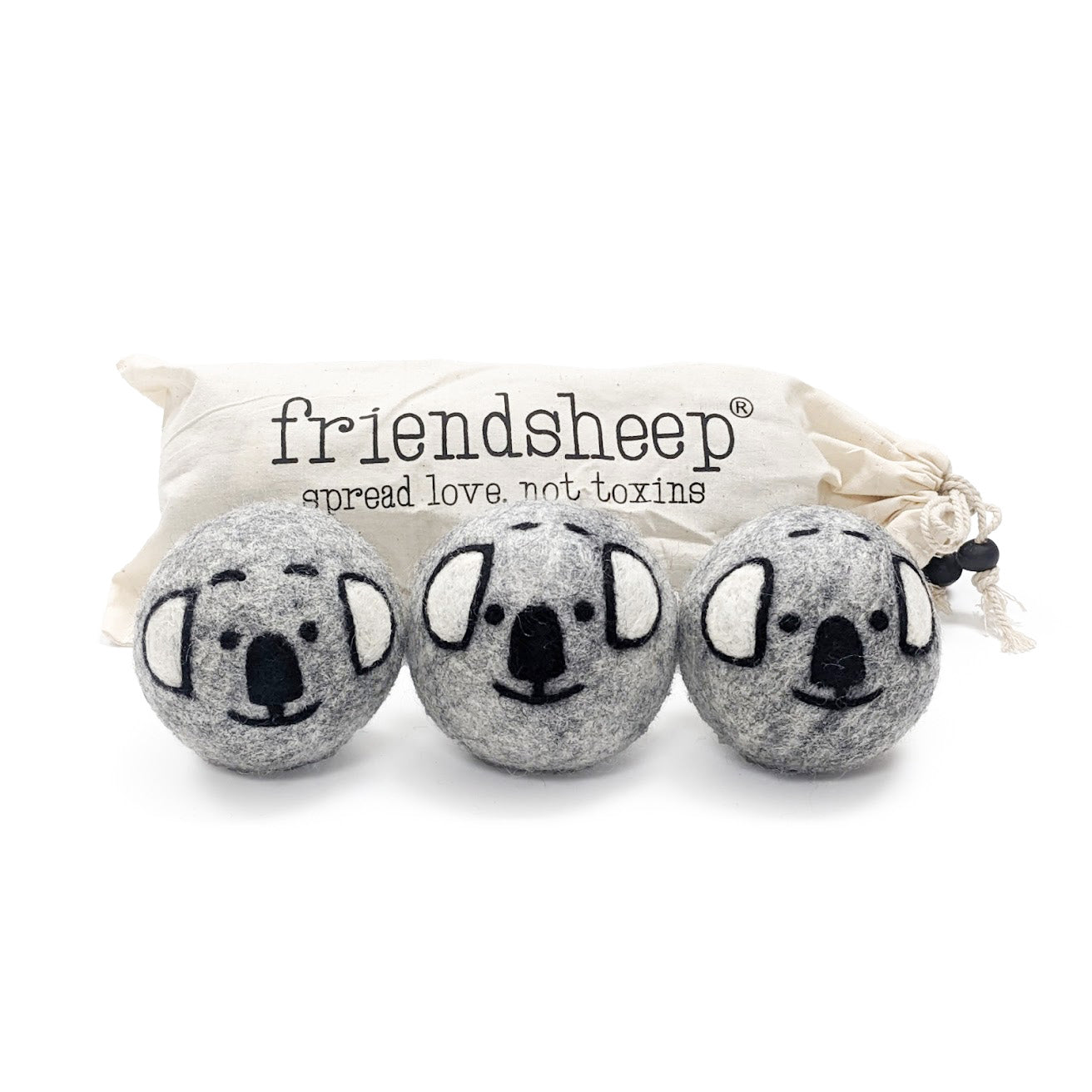 A set of three Friendsheep sustainable goods wool dryer balls are shown, decorated with a cute koala face. They are sitting in front of their white canvas drawstring bag.