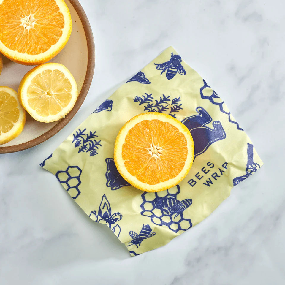 Slice of orange on beeswax wrap with bees, honeycombs, and bears design, surrounded by sliced lemons and oranges on a plate.