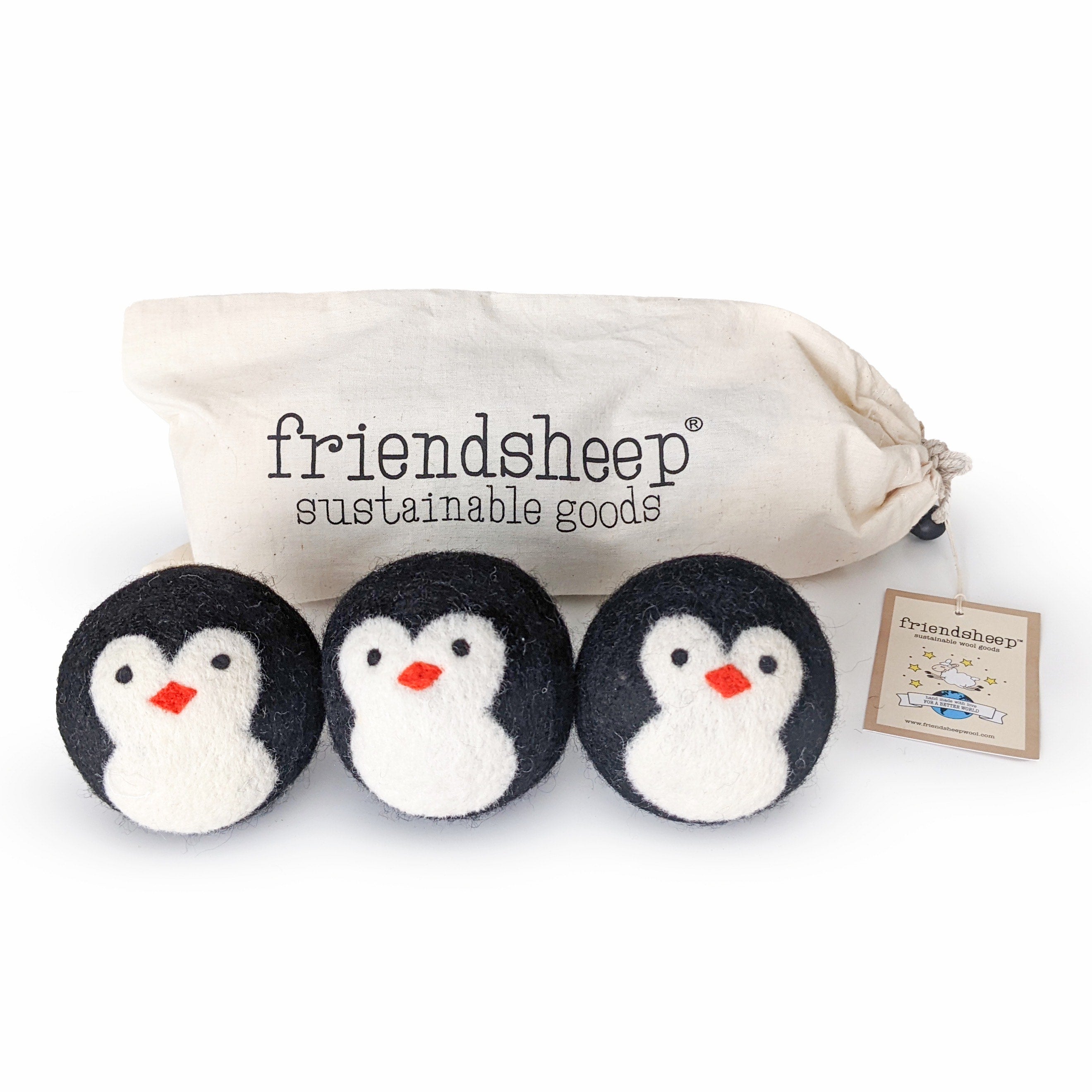 A set of three Friendsheep sustainable goods wool dryer balls are shown decorated with a cute penguin face. They are sitting in front of their white canvas drawstring bag.