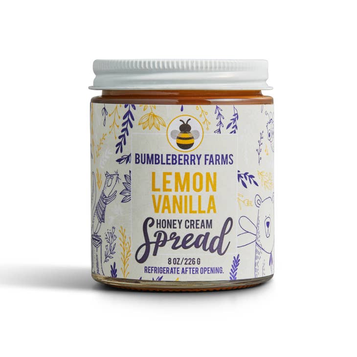 A jar of Bumbleberry Farms Lemon Vanilla Honey Cream Spread is shown. The clear glass jar has a white lid and a light beige label with a pattern of purple and yellow leaves and a bee icon. The label specifies the contents as an 8 oz. honey cream spread and includes instructions to refrigerate after opening.