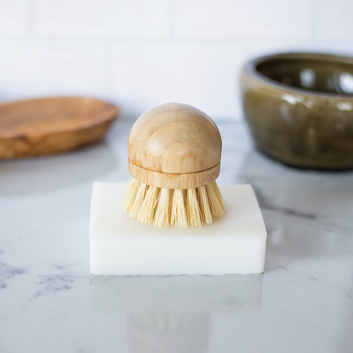 Natural white rectangular dish soap bar on a kitchen countertop with a bristle dish brush resting on top of the soap.