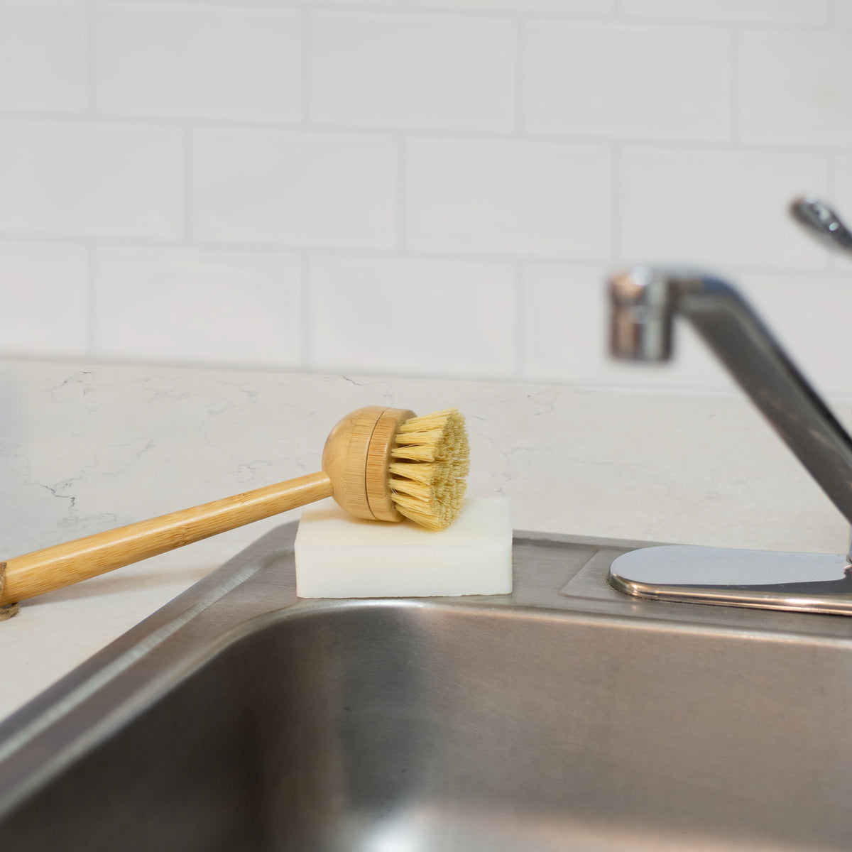 Natural white rectangular dish soap bar placed beside a kitchen sink with a bristle dish brush resting on top of the soap.