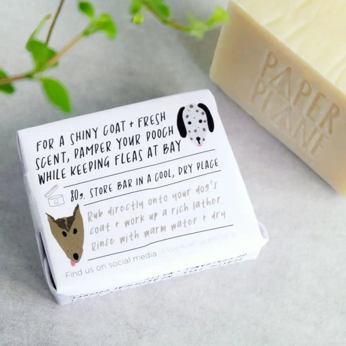 A small box of dog shampoo is shown, with text that describes its benefits, including a "shiny coat + fresh scent" and repelling fleas. A bar of soap from the same brand is blurred in the background.