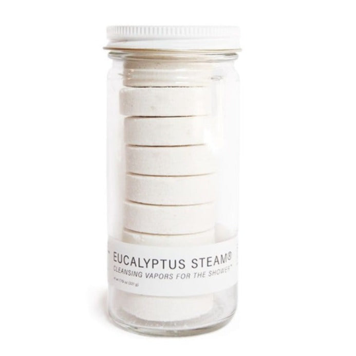A glass jar containing a stack of eight white, circular shower steamers. A label on the front of the jar reads "EUCALYPTUS STEAM. Cleansing Vapors for the shower.