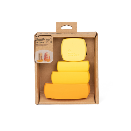 A brown, recyclable cardboard box displays a set of four reusable silicone food wraps in a clear plastic window. The wraps are shaped like cheese wedges and are arranged in a stack, with a gradient of colors from pale yellow to bright orange. A playful tagline inside the box reads, "if you love your food, give it a hug" which speaks to the product's purpose as a reusable "Cheese Hugger".