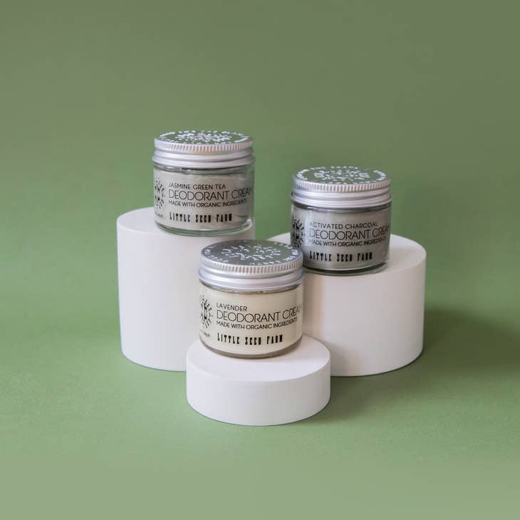 This image is a product shot showing three different scents of Little Seed Farm deodorant cream displayed on white cylindrical pedestals. From top to bottom, they are Jasmine Green Tea, followed by Activated Charcoal scent and at the smaller pedestal, Lavender.