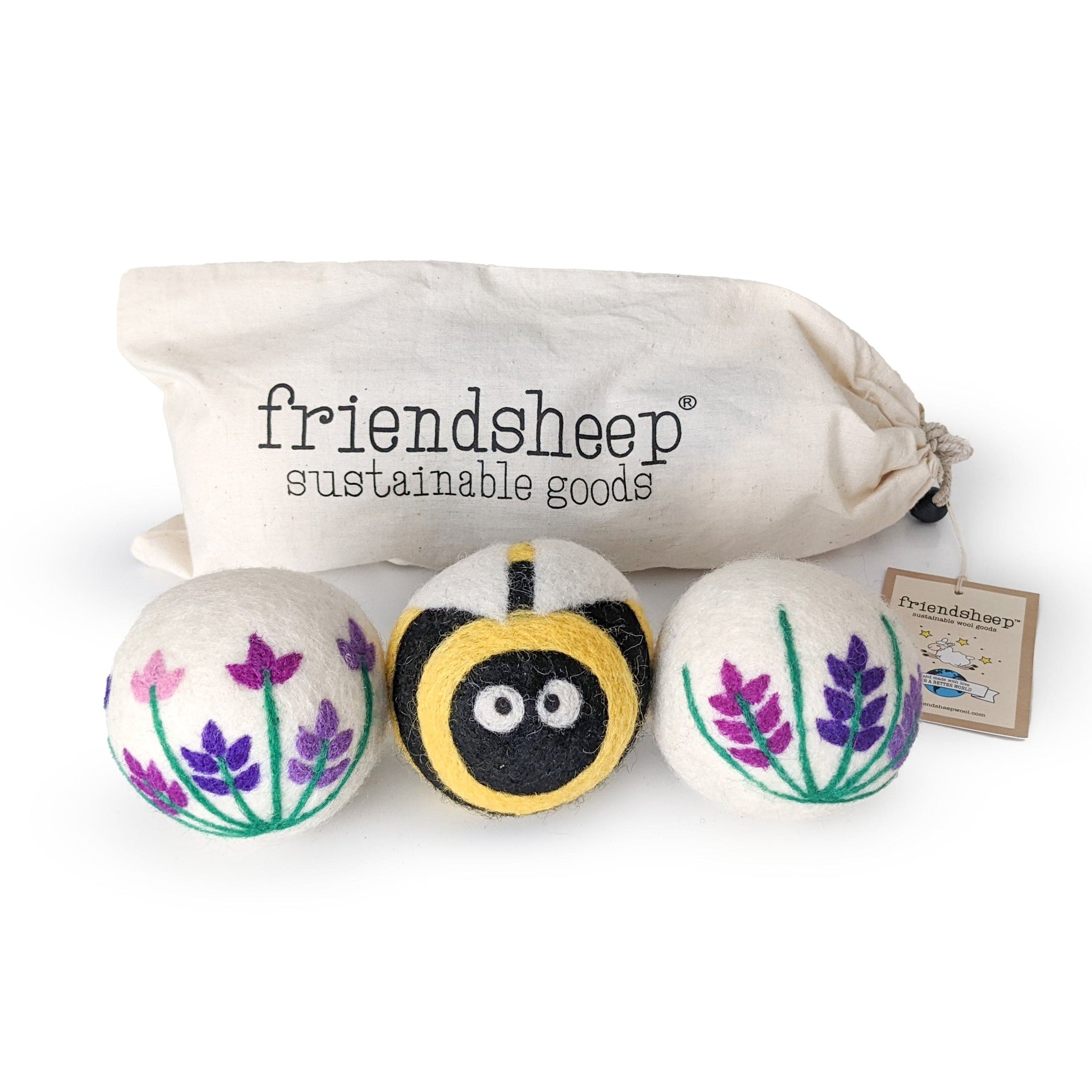 A set of three Friendsheep sustainable goods wool dryer balls are shown, decorated with a cute bee and two floral designs. They are sitting in front of their white canvas drawstring bag.
