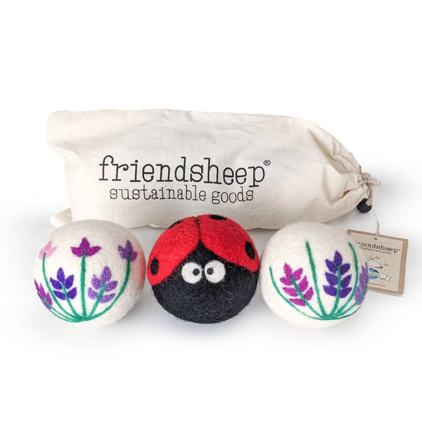 A set of three Friendsheep sustainable goods wool dryer balls are shown, decorated with a cute ladybug and two floral designs. They are sitting in front of their white canvas drawstring bag.