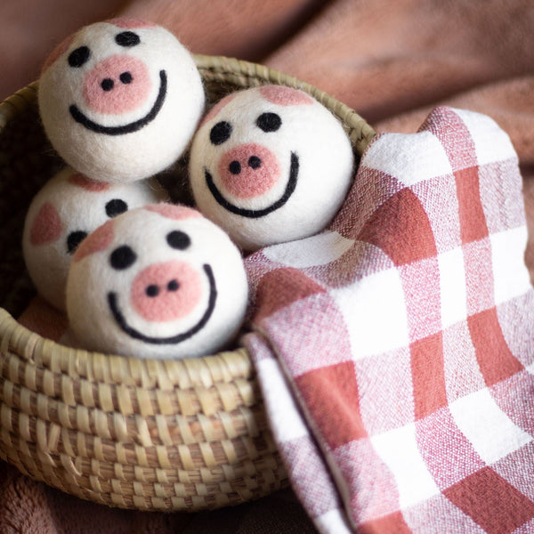 Piggy Band wool dryer balls in burgundy and white, arranged in a basketon on a folded burgundy and white checkered towel