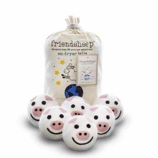 Six wool dryer balls designed as pink pigs with black details, arranged with a natural cotton drawstring bag on a neutral background. Made from 100% organic New Zealand wool to naturally soften clothes and reduce drying time.