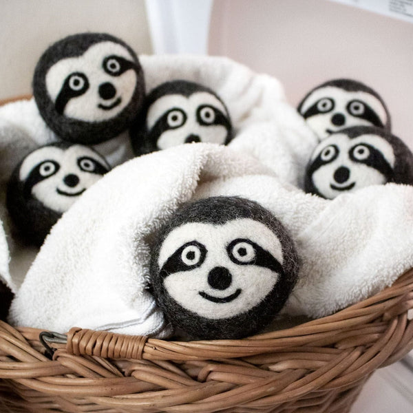 Sloth Squad wool dryer balls featuring raccoon designs resting in a basket with a white towel.