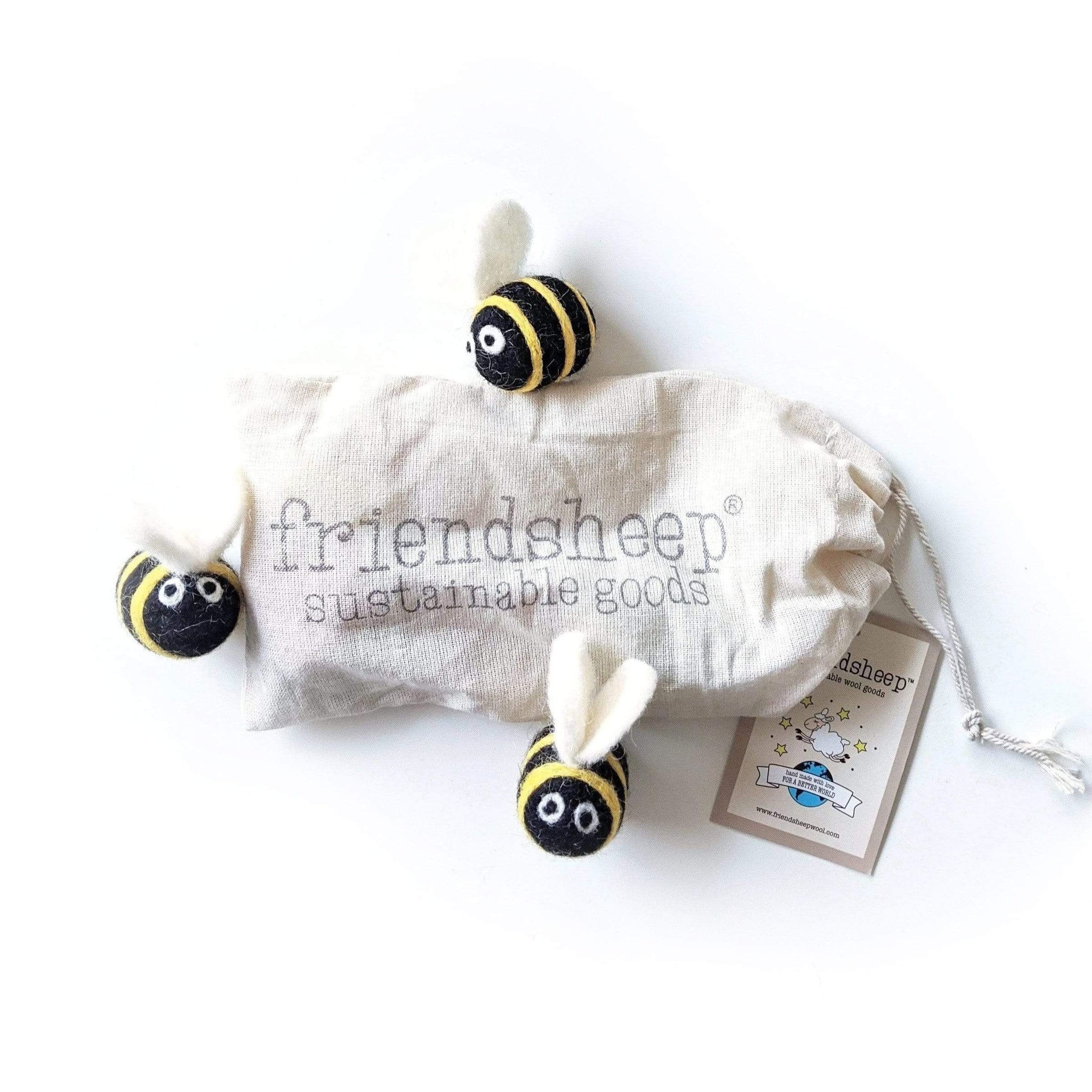 Three felted wool bees are arranged around a "friendsheep sustainable goods" cloth drawstring bag. The bag and its attached tag also feature the "friendsheep" brand name.