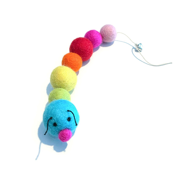 A felted wool toy is shown, consisting of a string of colored balls with a bell at the end. The first ball is blue with a pink nose and black eyes, followed by balls in a rainbow pattern.