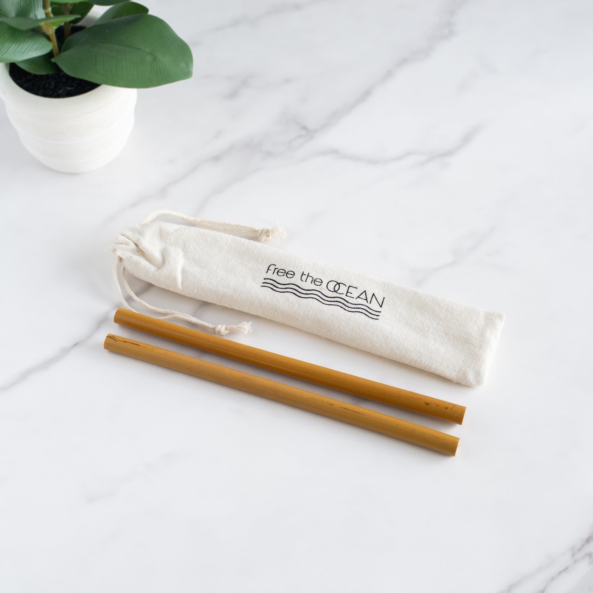 A cloth carrying bag with a "Free the OCEAN" logo and two reusable bamboo straws lie on a white marble countertop.