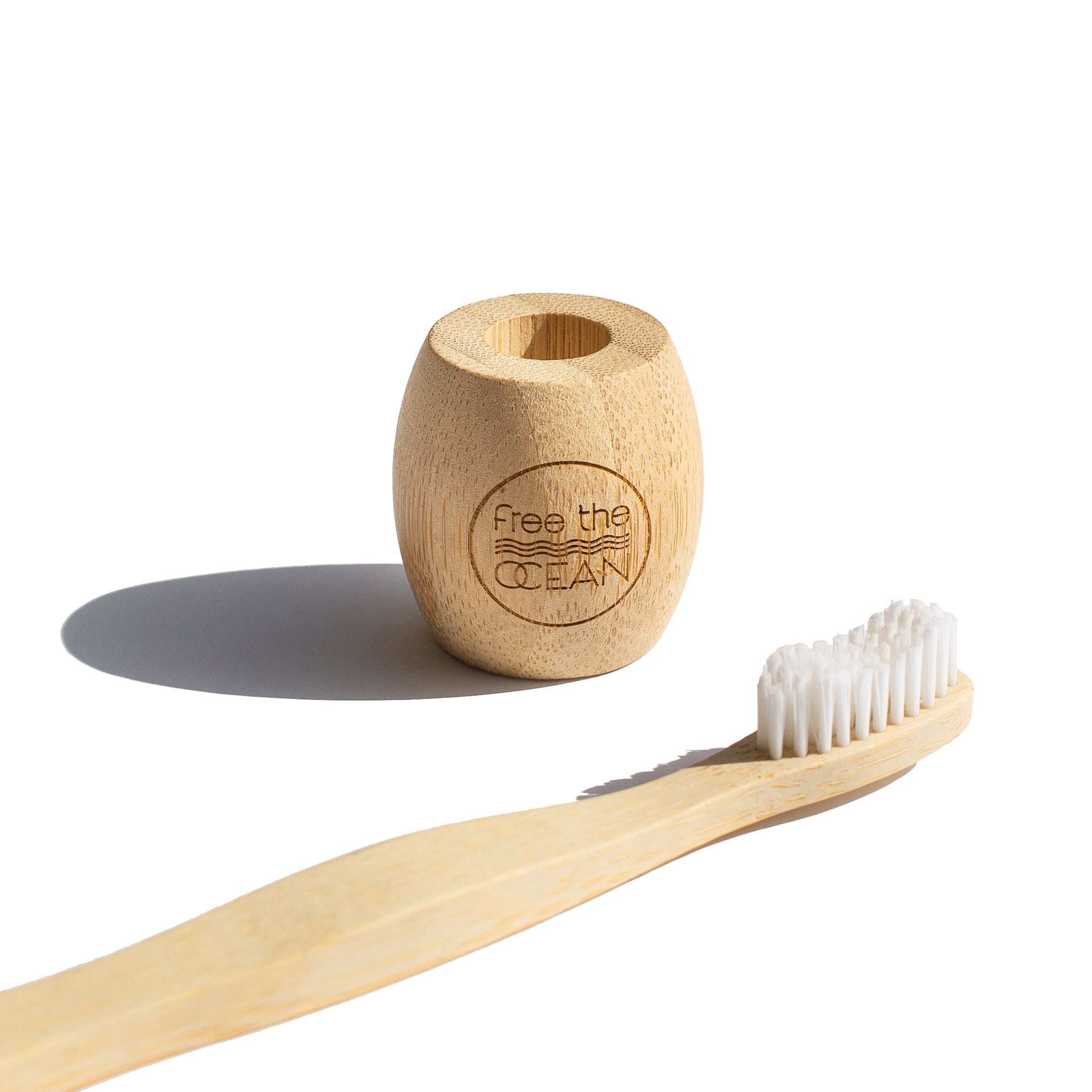 A bamboo toothbrush and a matching bamboo holder with the words "Free the OCEAN" engraved on it are shown on a white background.