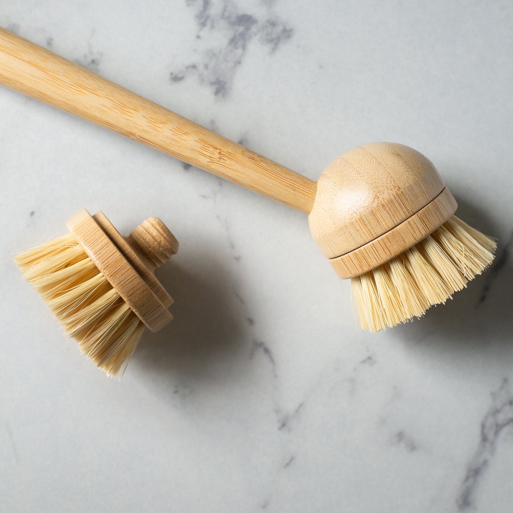 Wooden dish brush with bamboo handle and replacement brush head placed side by side on a gray surface.