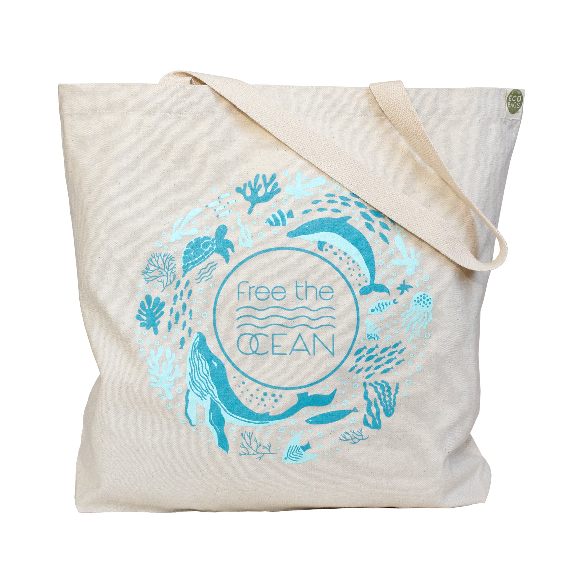 A beige canvas tote bag features a large circular logo in teal-blue, showing a whale and a dolphin swimming among various other sea creatures. The center of the logo reads "Free the OCEAN"