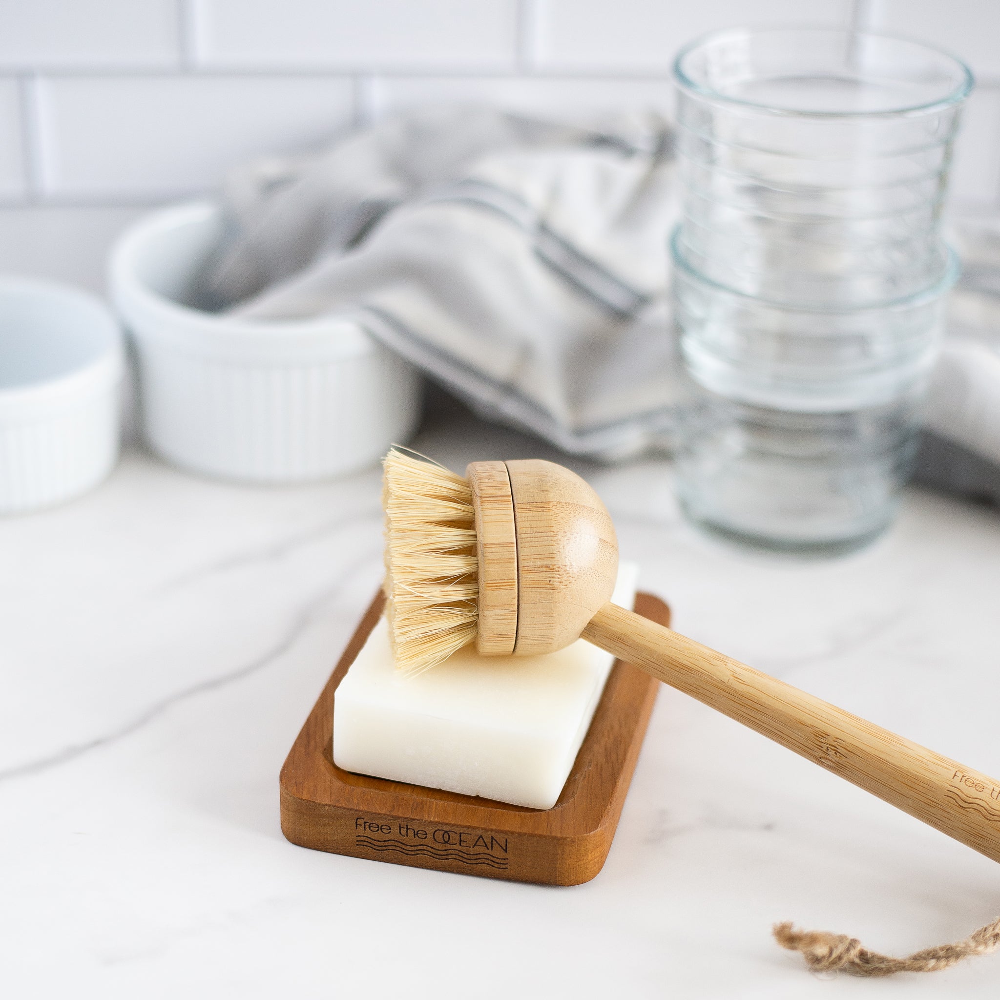Wooden dish brush resting in a soap dish next to a vegan dish soap bar, styled in a kitchen setting.