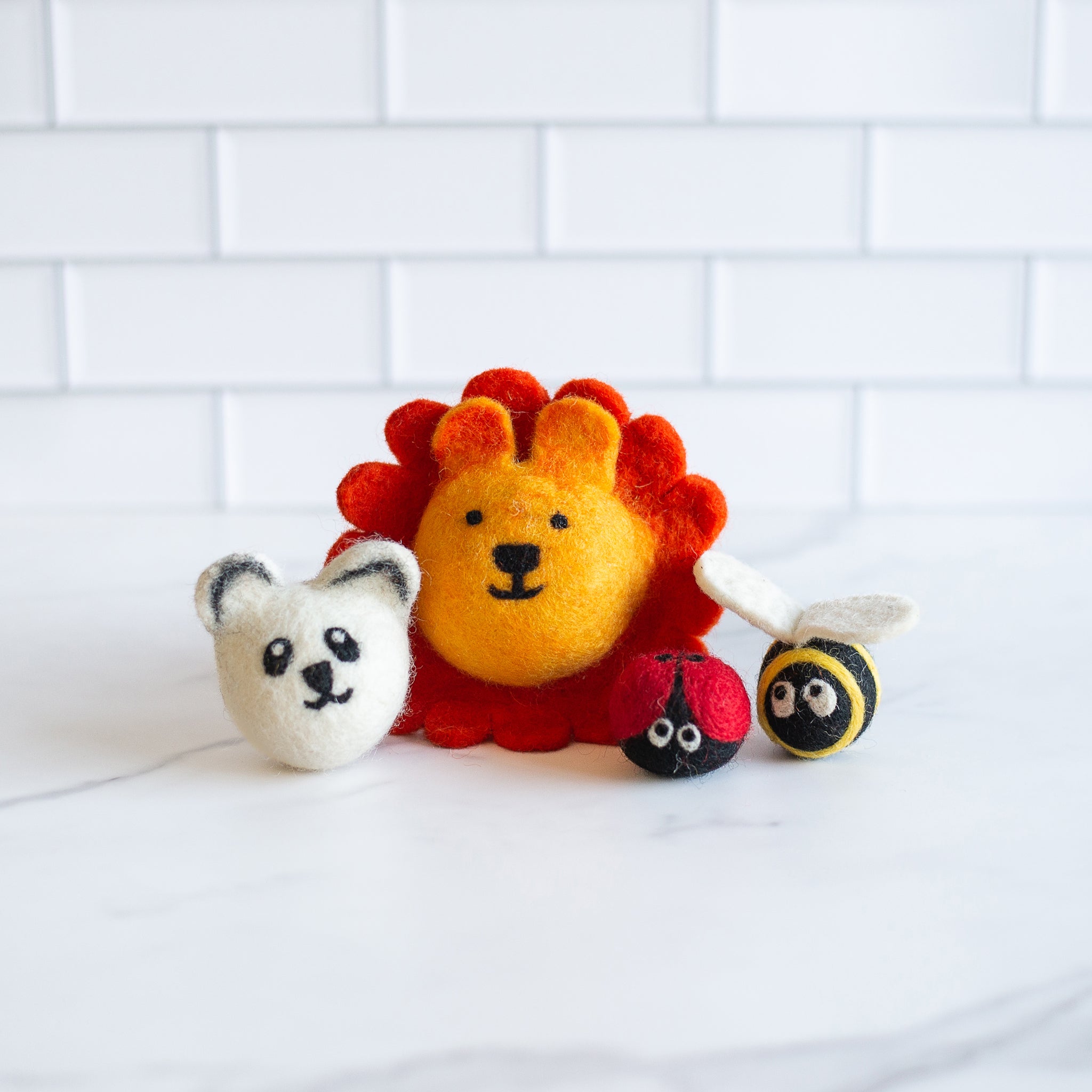 Four wool cat toys—including a panda, lion, bee, and sloth—resting on a textured cream surface with soft shadows, showcasing handmade detail and natural materials.