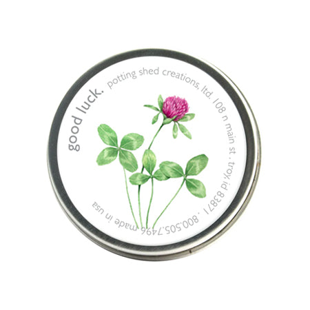 A silver tin of garden sprinkles with a white label on the lid. The label features a watercolor illustration of a four-leaf clover and a pink clover flower, with the text 'good luck, potting shed creations' around the edge.
