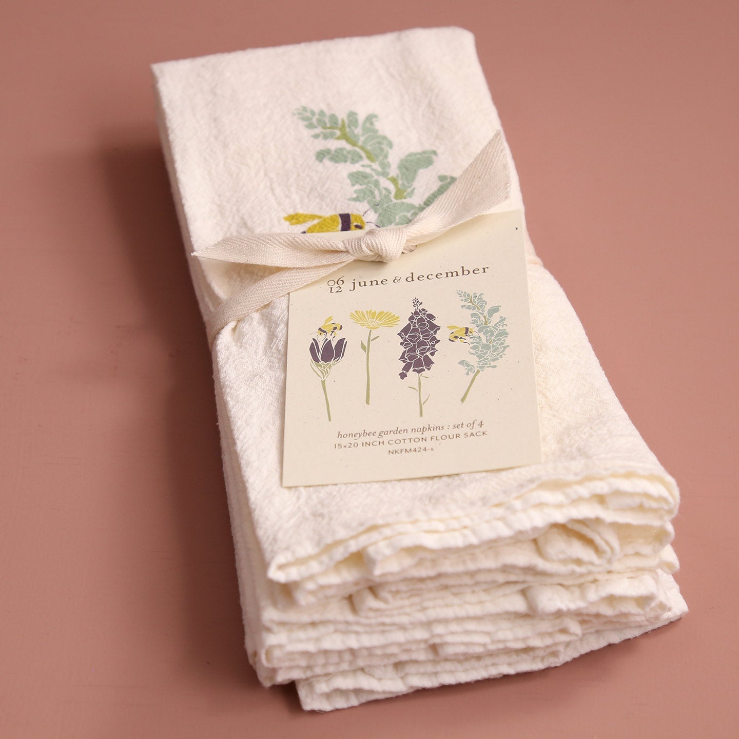 A sweet set of four "honeybee garden napkins" from "june & december" is stacked and tied with a ribbon. The white tag shows illustrations of the four different bee and floral designs included in the set.