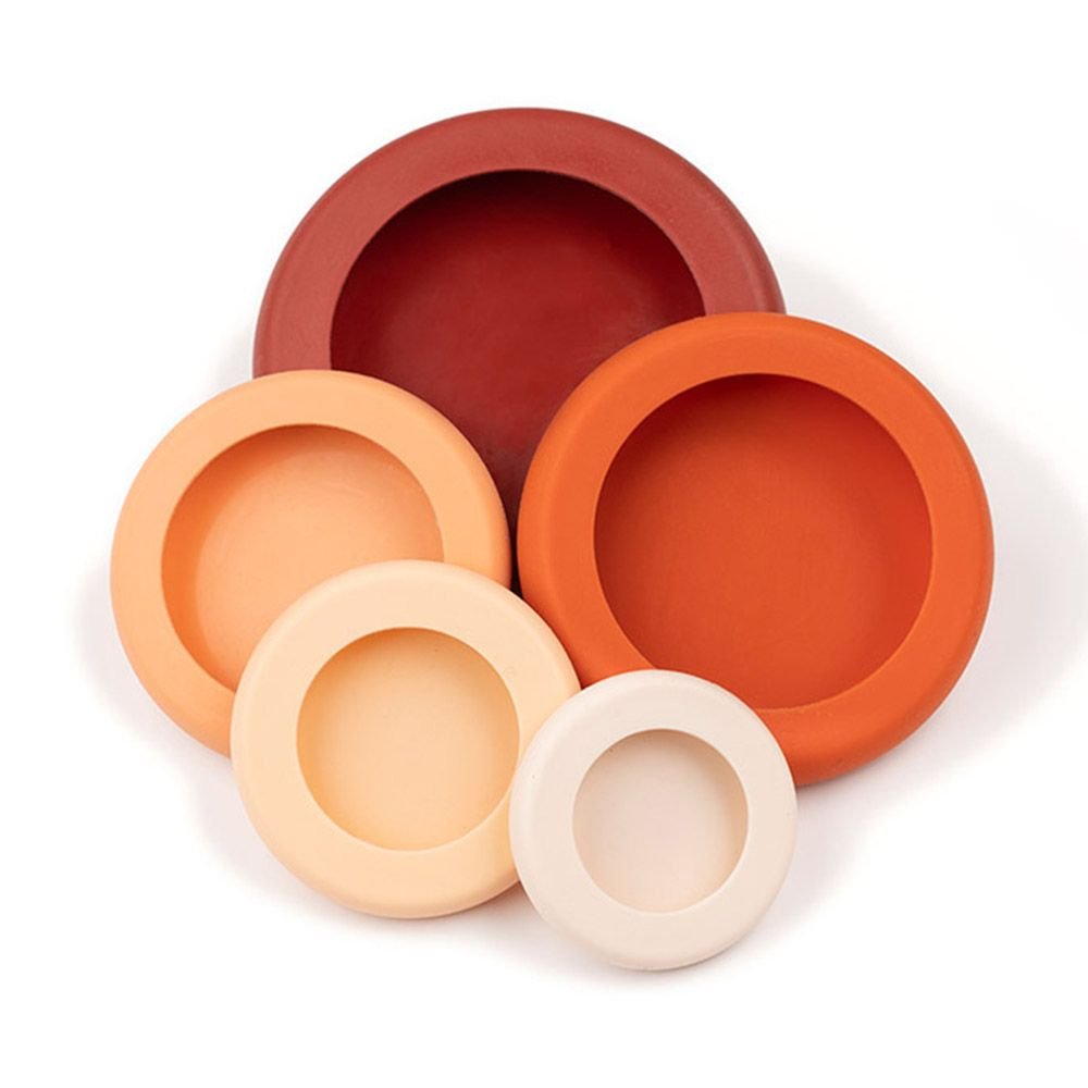A set of 5 sizes reusable silicone food savers in a stack. The savers come in a gradient of earthy tones, including off-white, orange and red.