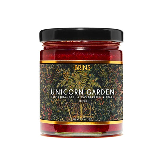 A jar of red-colored Brins Unicorn Garden spread is shown on a white background. The label identifies the spread as a combination of pomegranate, strawberries and rose. The jar has a dark, decorative label with a botanical pattern.