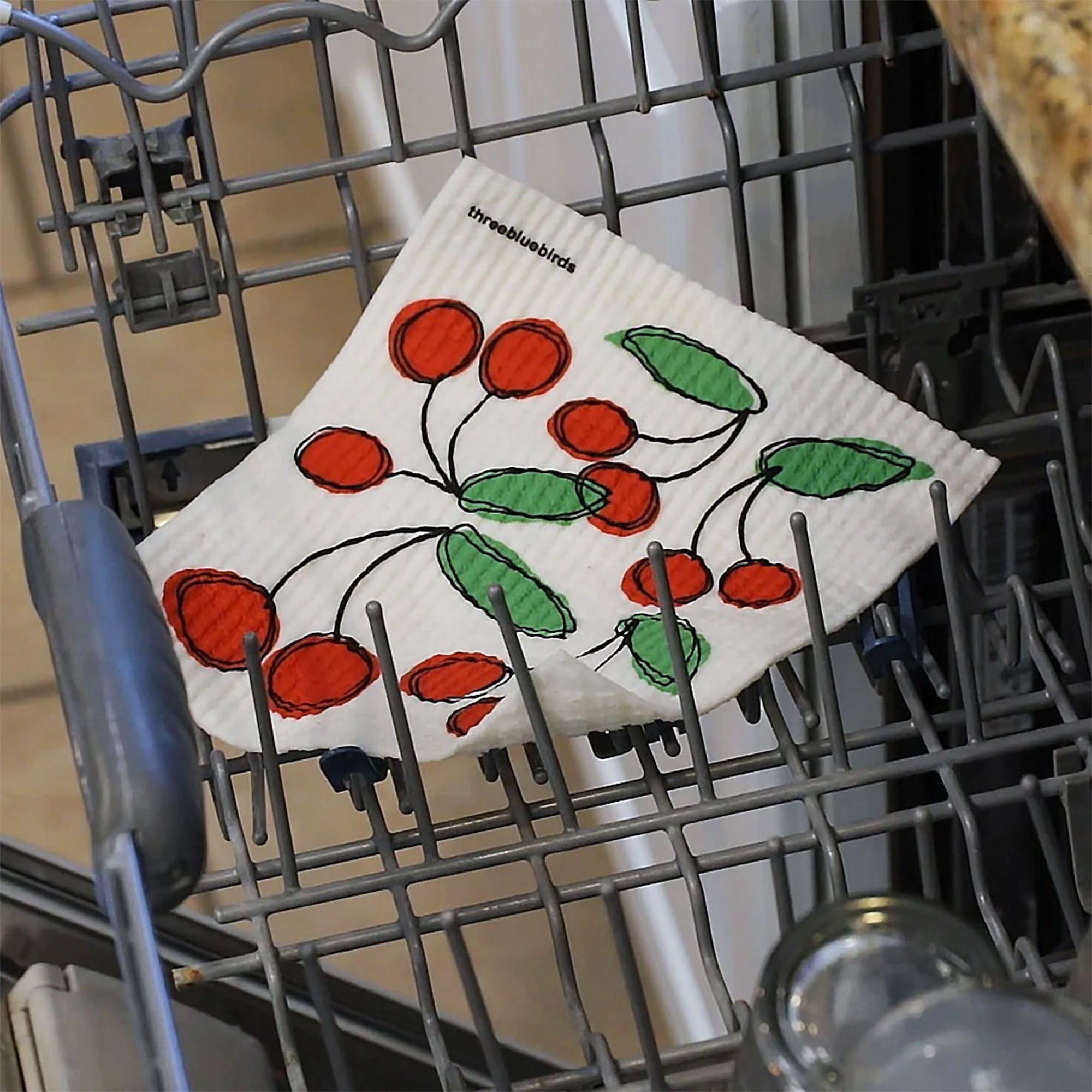 A lifestyle image showing reusable Swedish dishcloths with a vibrant red cherry pattern inside a dishwasher, highlighting their washability and reusability.