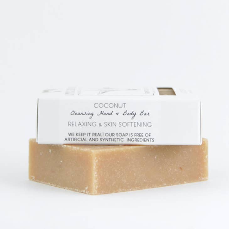 A creamy bar of Little Seed Farm soap rests on a white surface with its packaging behind it.