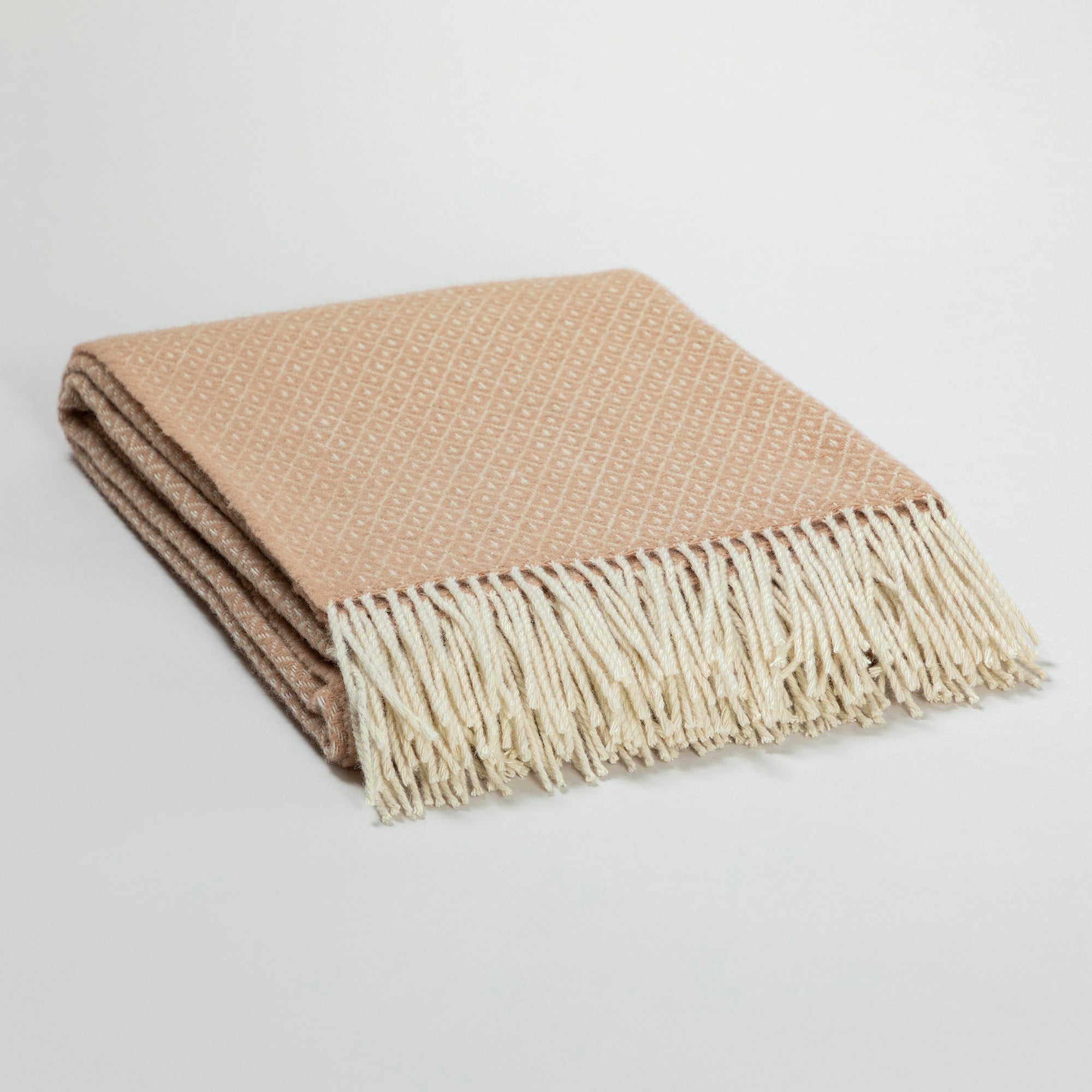 Close-up detail of the peach Ukrainian blanket’s diamond weave pattern and soft cream fringe, showing the texture and quality of the wool fabric. One corner of the blanket is gently folded over.