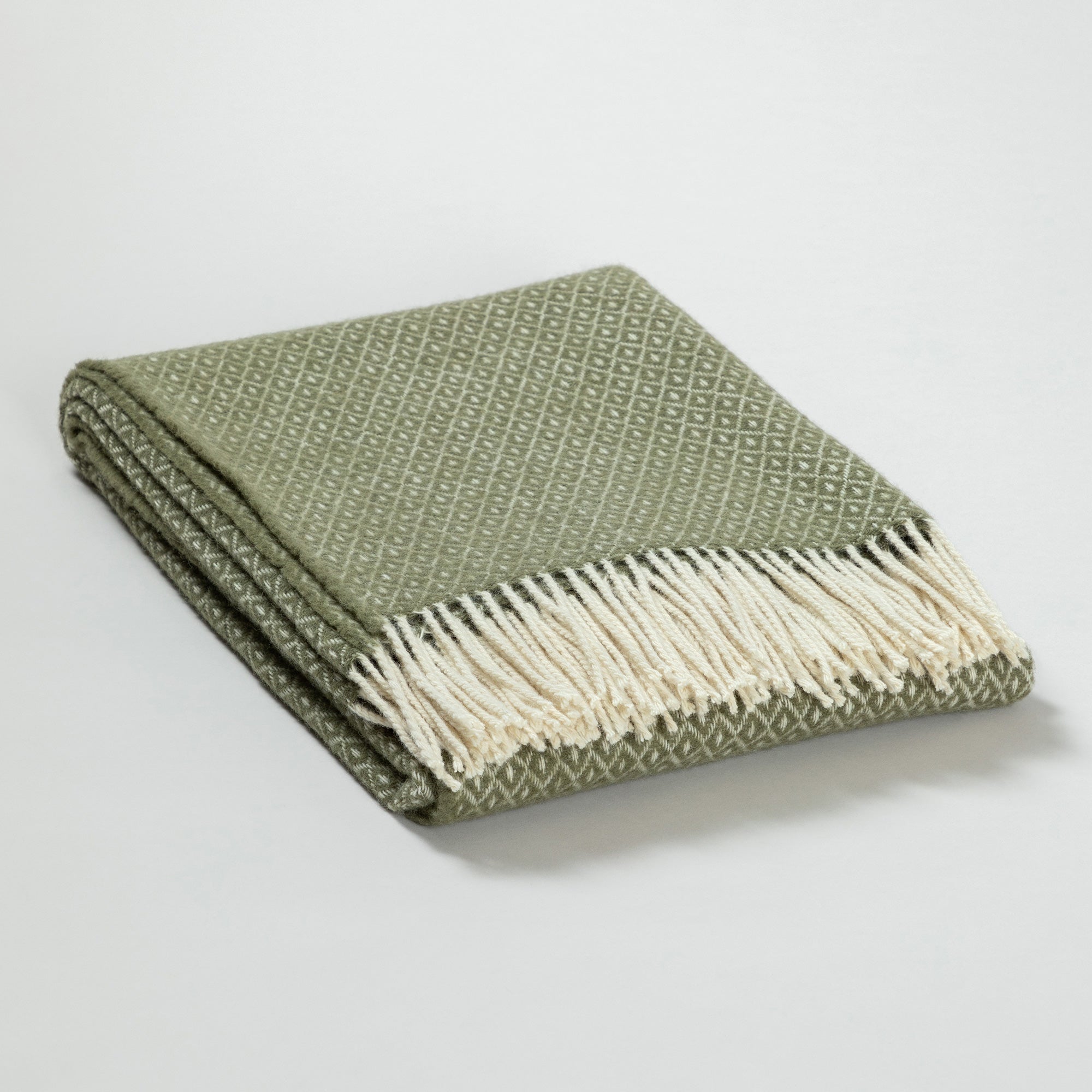 Folded olive green and cream diamond-patterned Ukrainian blanket with cream fringes, neatly folded on a white background.