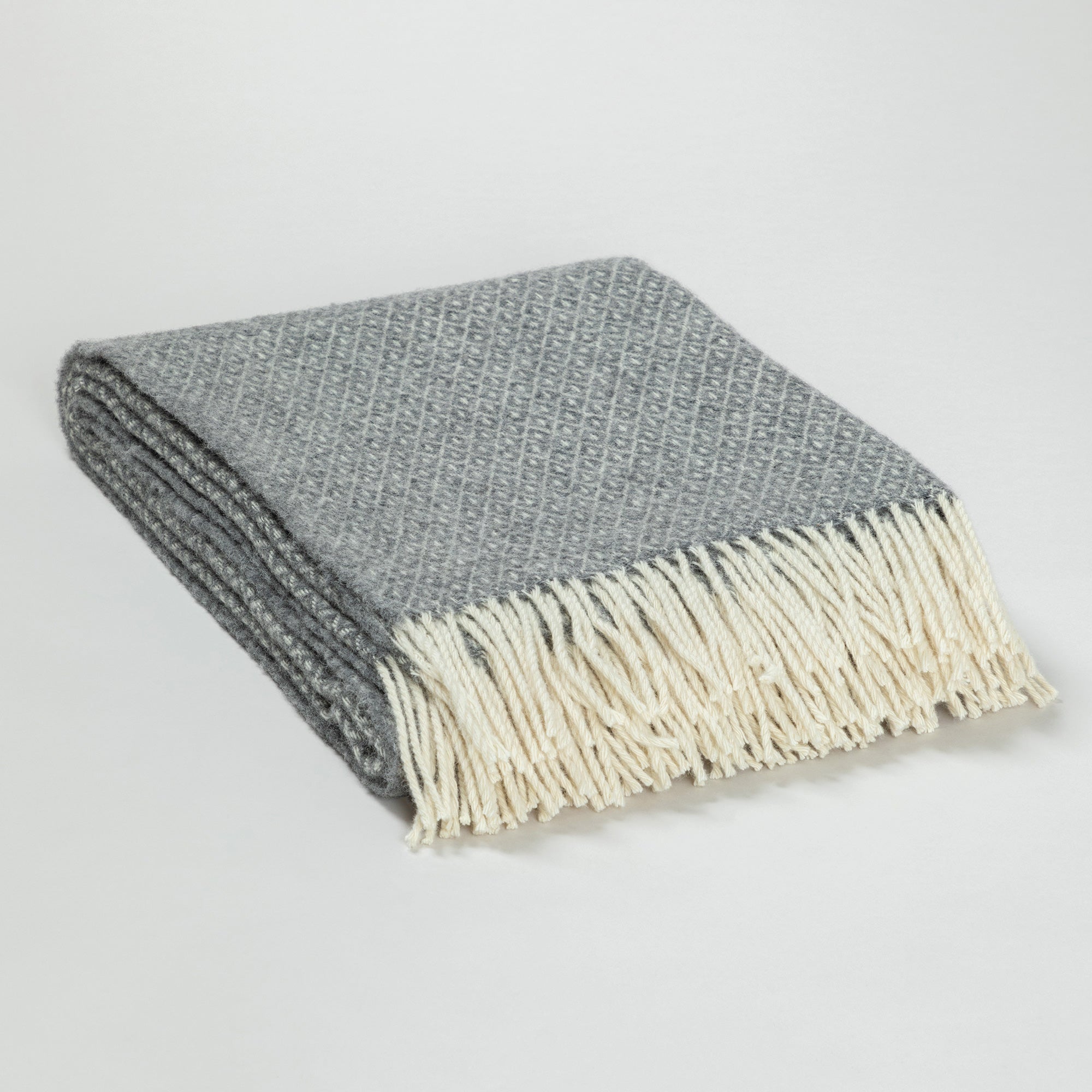 Close-up photo of a folded gray blanket with a small diamond pattern and cream-colored fringe, displayed on a white surface.