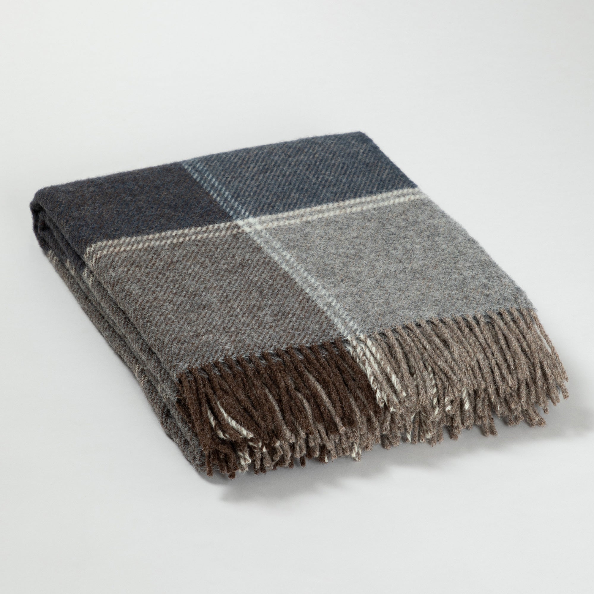 Folded wool throw blanket with plaid patterns in shades of gray, brown, and blue, featuring fringed edges on a white background.
