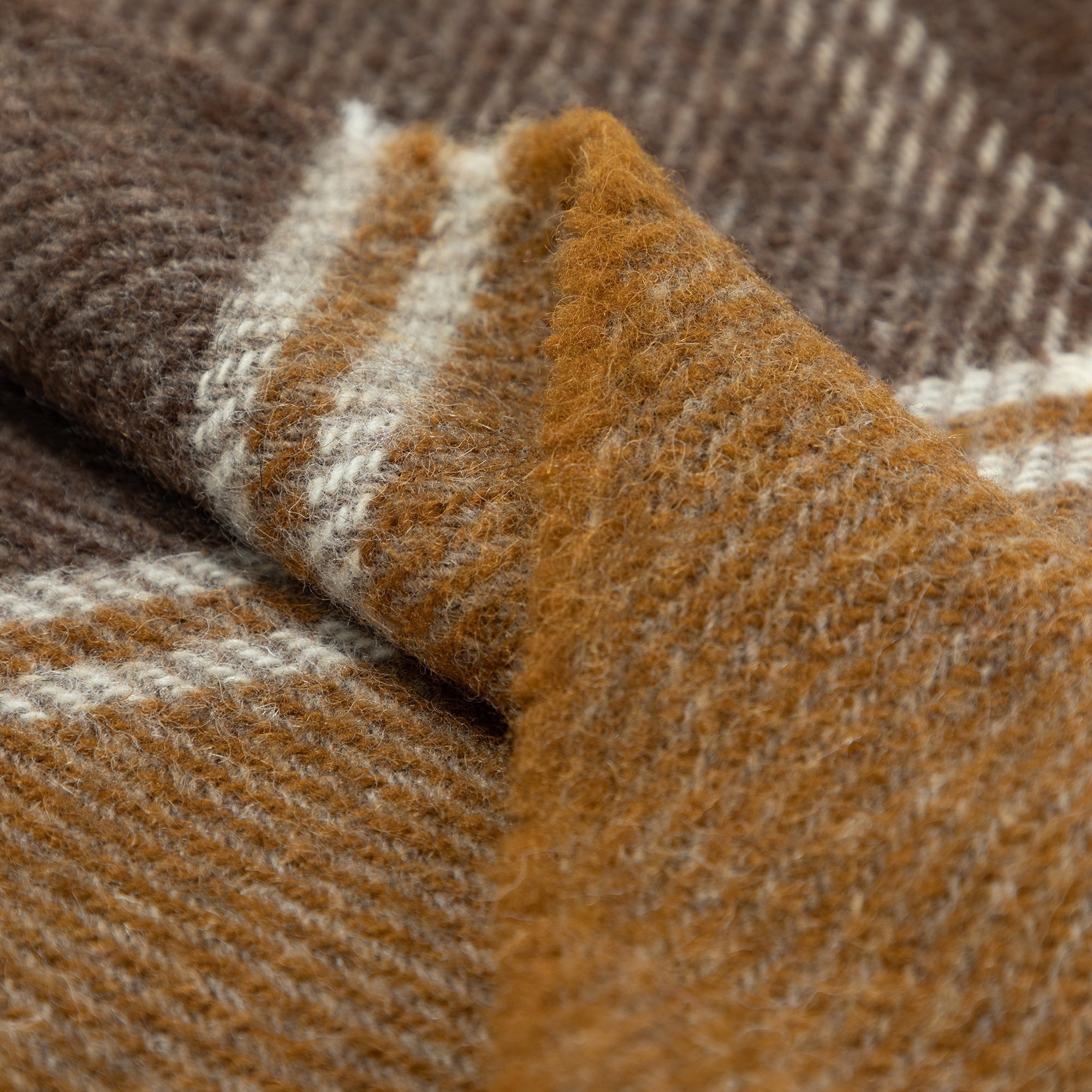 Close-up of folded wool throw blanket with plaid patterns in brown, mustard yellow, and cream, showing soft texture and fibers.