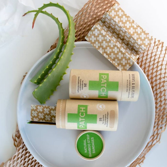 Two kraft cardboard tubes of Aloe Vera biodegradable bandage strips resting on a ceramic dish, styled with aloe branches.